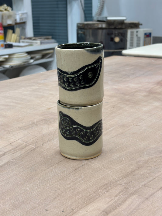 White ceramic cup, glossy black interior, and a black snake illustration on the exterior. Stamped with LKBK maker’s mark.