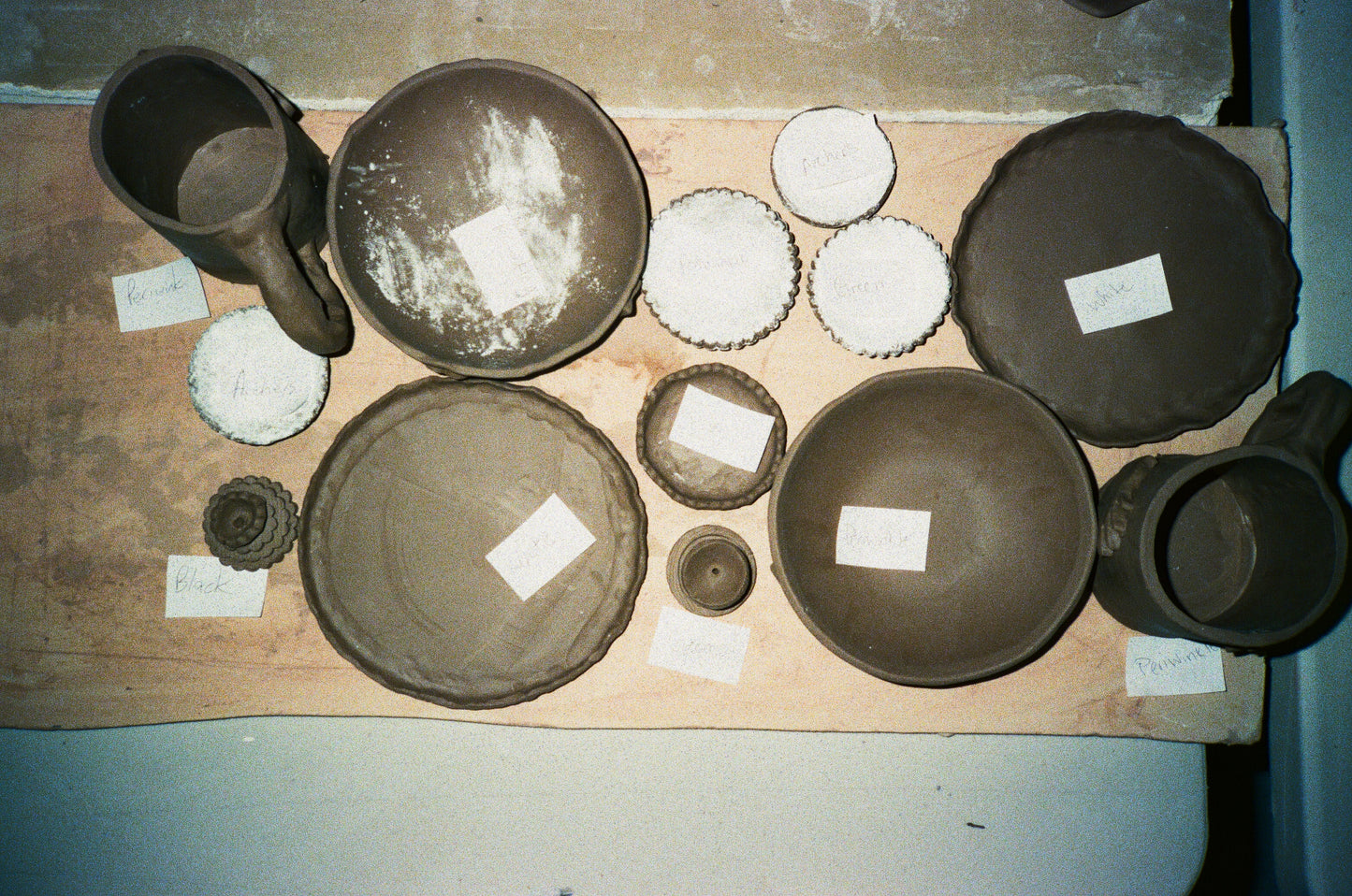 Grainy film image of various clay plates, mugs, and incense burners made out of dark and light clay.