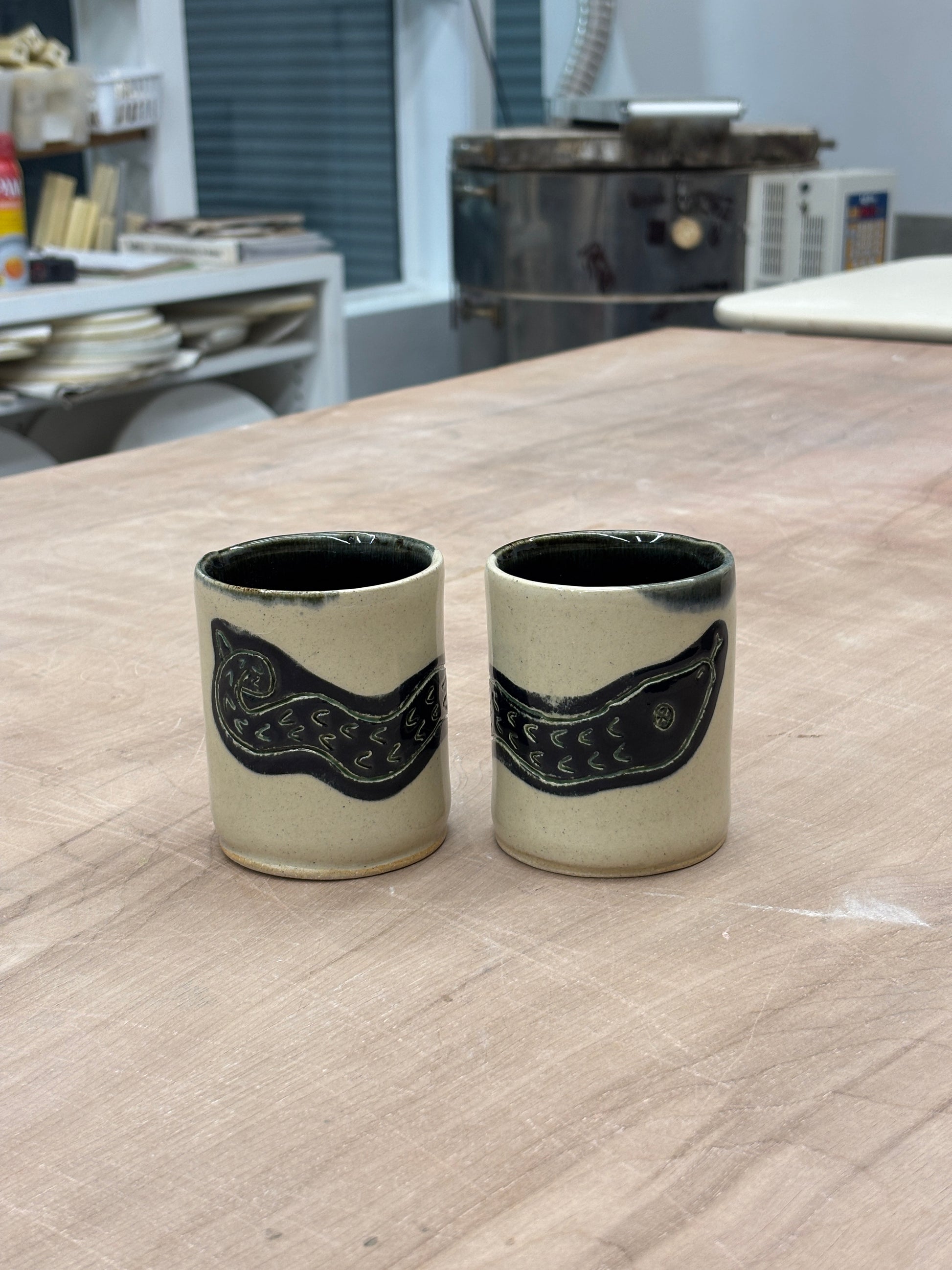 White ceramic cup, glossy black interior, and a black snake illustration on the exterior. Stamped with LKBK maker’s mark.