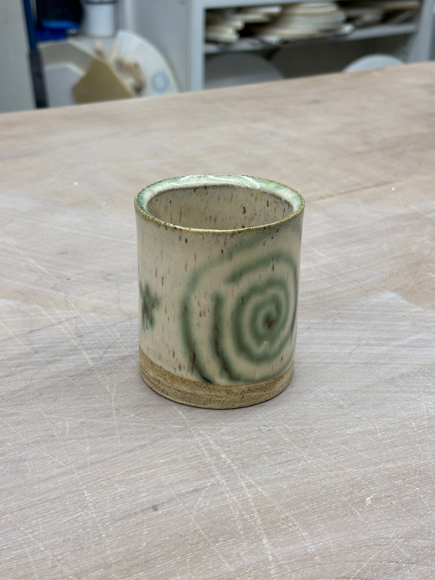 Speckled ceramic cup with a cream glaze. Melty swirls and stars in green copper adorn the outside. Stamped with LKBK maker’s mark on the bottom.