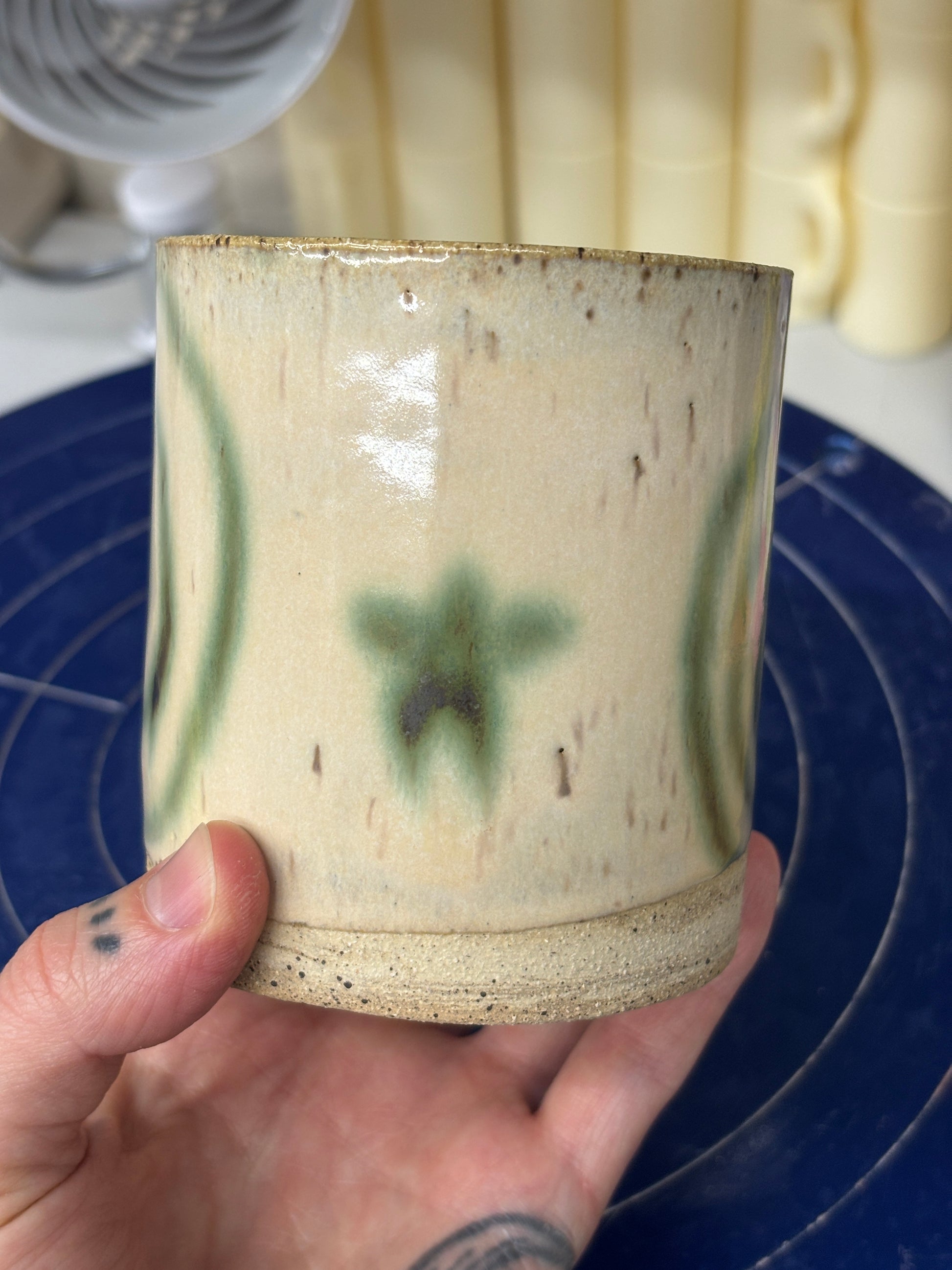 Speckled ceramic cup with a cream glaze. Melty swirls and stars in green copper adorn the outside. Stamped with LKBK maker’s mark on the bottom.